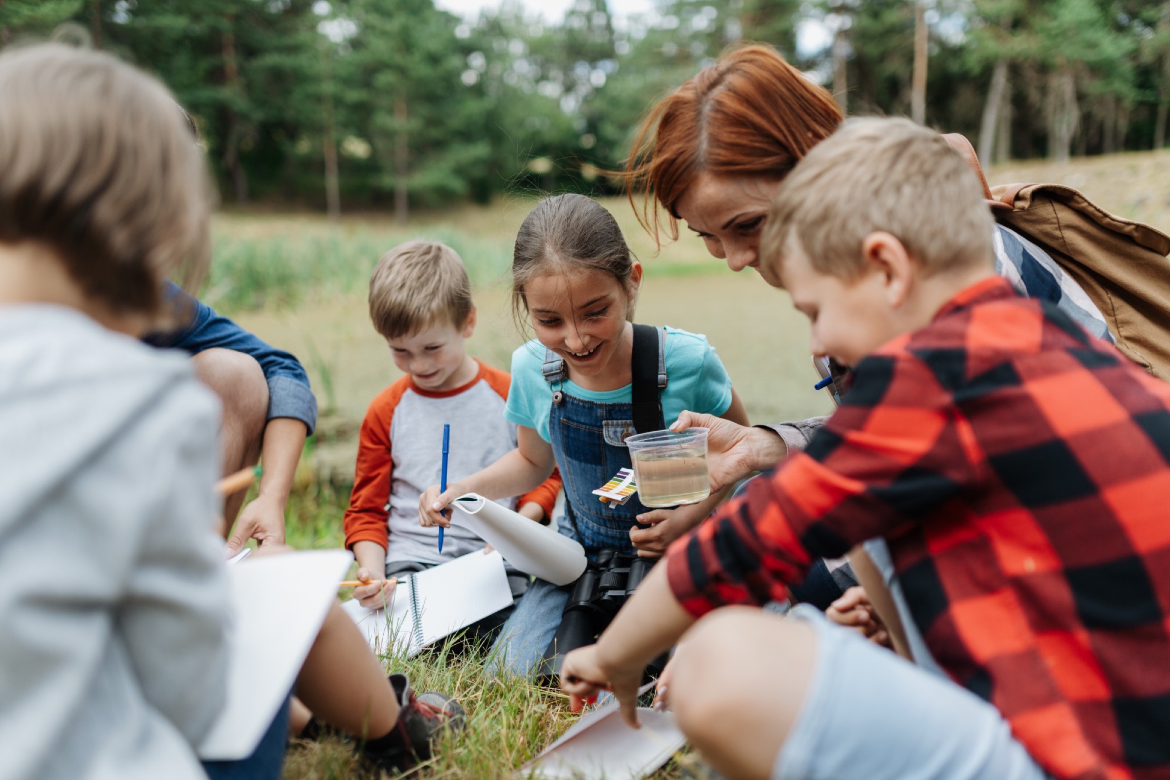 A teacher and students testing pond water outdoors