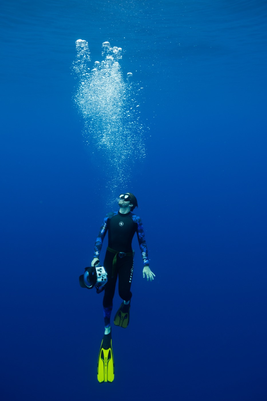 A scuba diver rises through blue water and bubbles