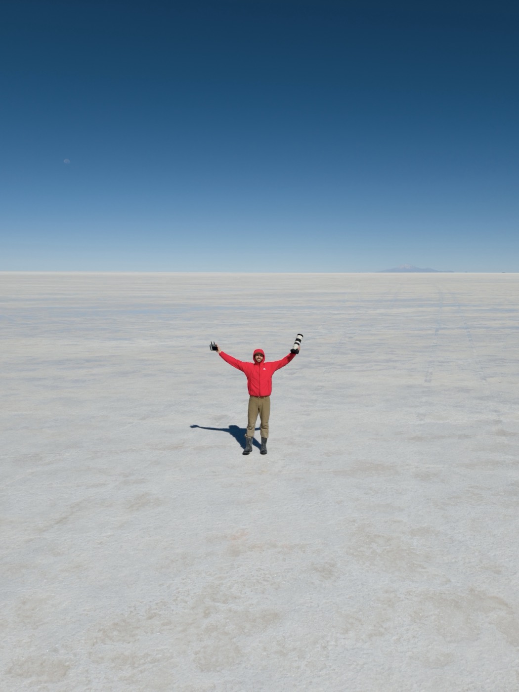 A person in red stands on a vast reflective salt flat