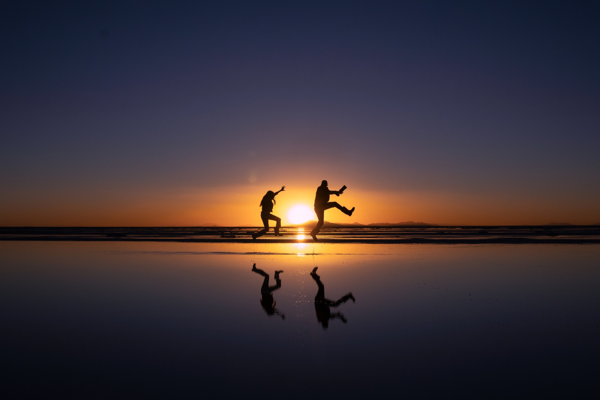 Two people leap against a sunset over still water